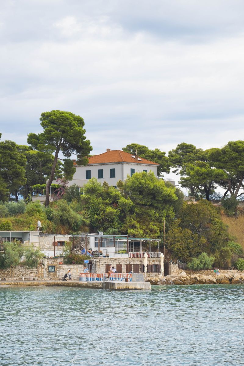 A picturesque coastal scene with trees and a mansion in Split, Croatia.