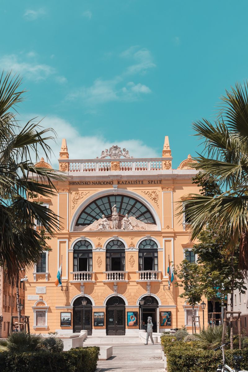Stunning view of the Croatian National Theatre in Split on a sunny day, framed by palm trees.