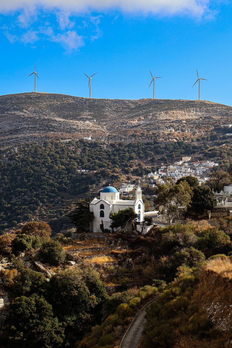 Scenic view of a white church in Greek landscape with wind turbines in the background.