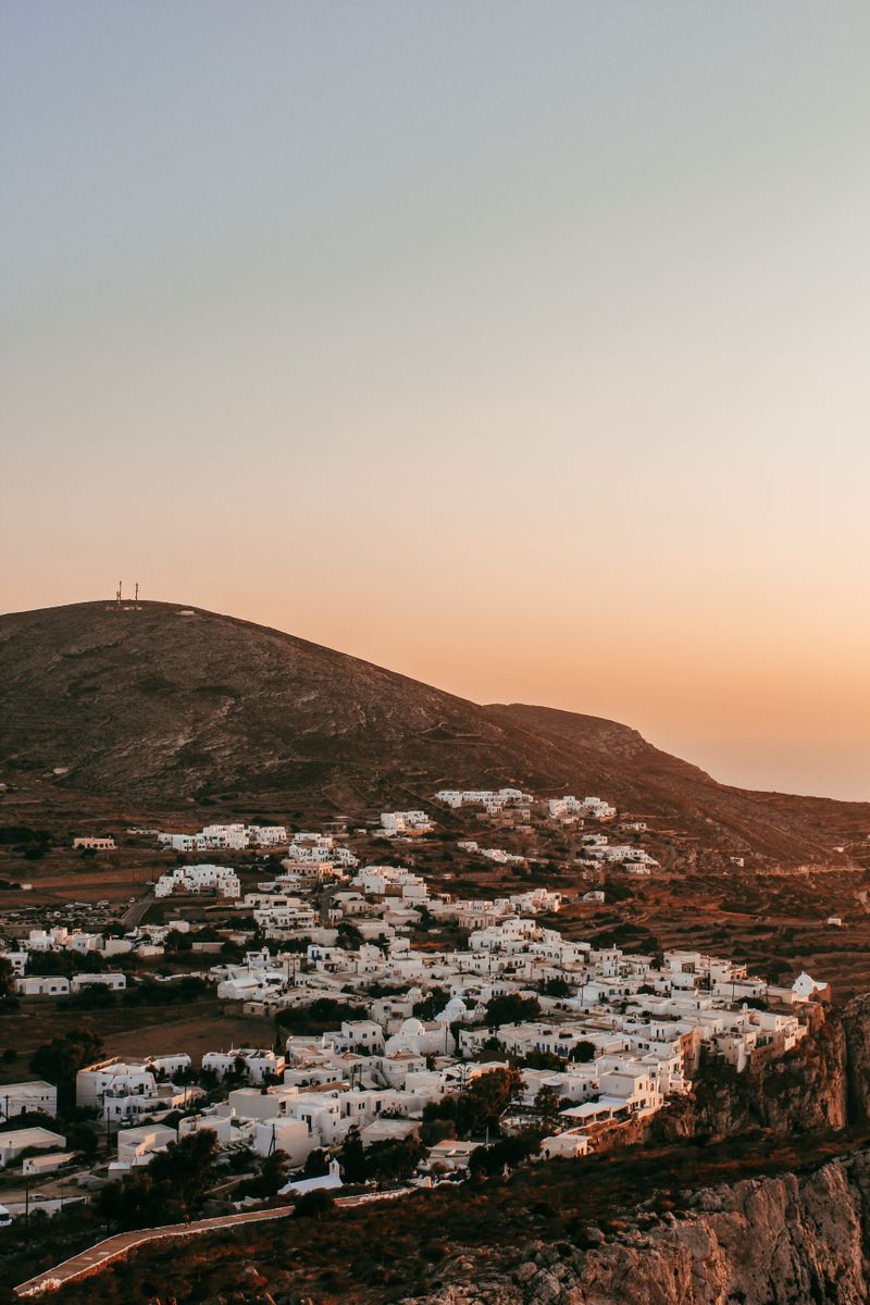 Stunning view of a whitewashed hillside village in Folegandros at sunset, capturing serene Greek island beauty.