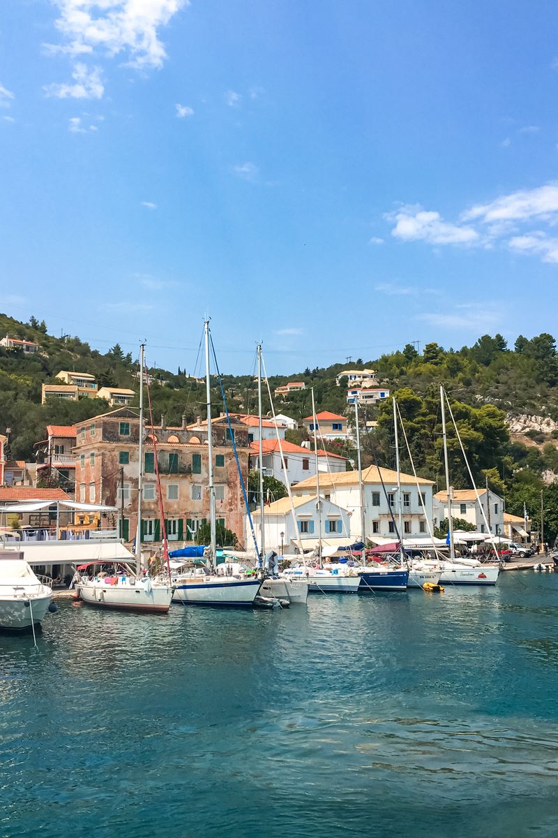 Picturesque Greek harbor with sailboats and traditional buildings under a blue summer sky.