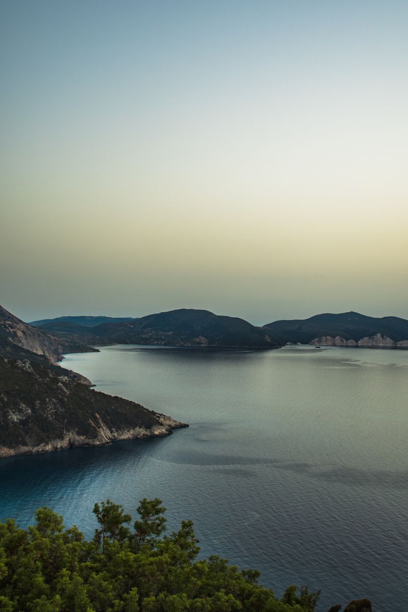 A serene view of the Greek coastline at dusk, showcasing peaceful waters and distant hills.