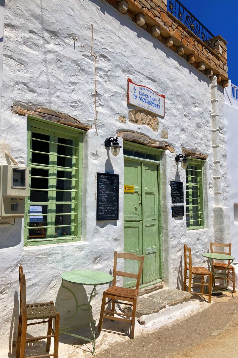 Traditional Greek cafe exterior in Aegiali with tables and chairs.