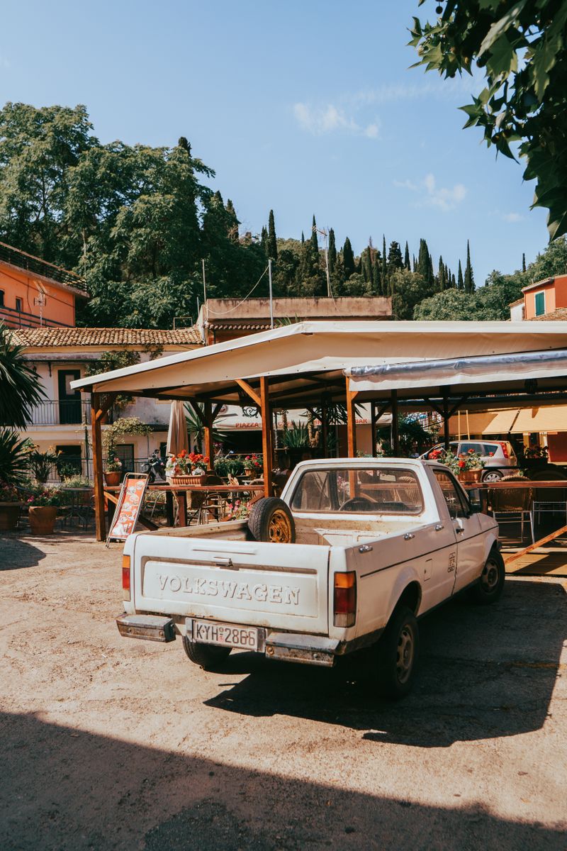 Vintage Volkswagen pickup truck in a quaint street scene in Kerkyra, Greece, under a bright summer sky.