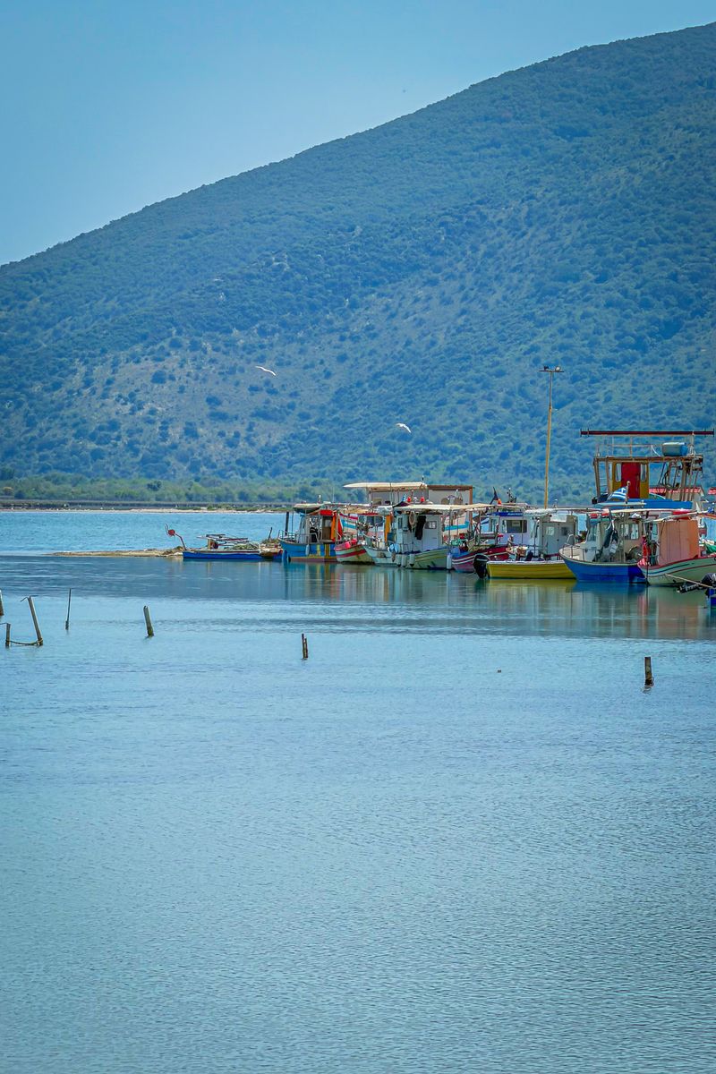 Tranquil fishing village by the sea with boats and mountains under a clear blue sky.