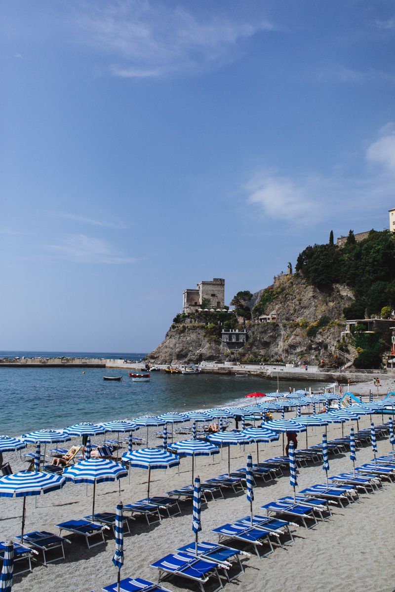 Plenty of similar sunbeds with parasols on sandy shore near rocky formation in resort