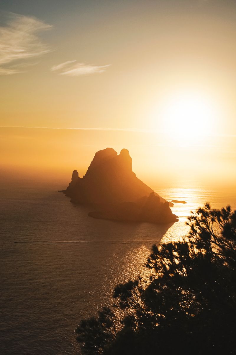 A breathtaking view of the sunset over the iconic Es Vedrà island, reflecting on calm ocean waters.