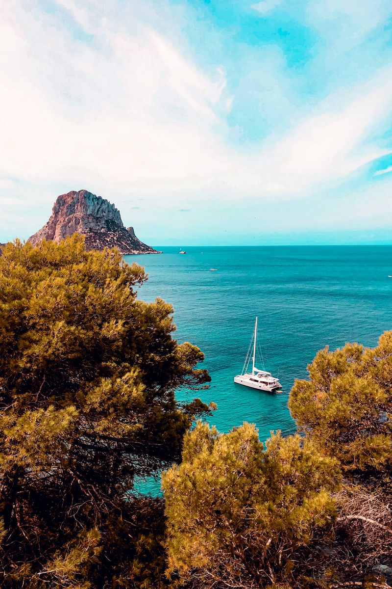 Breathtaking view of a yacht sailing near a rocky island, surrounded by lush trees.