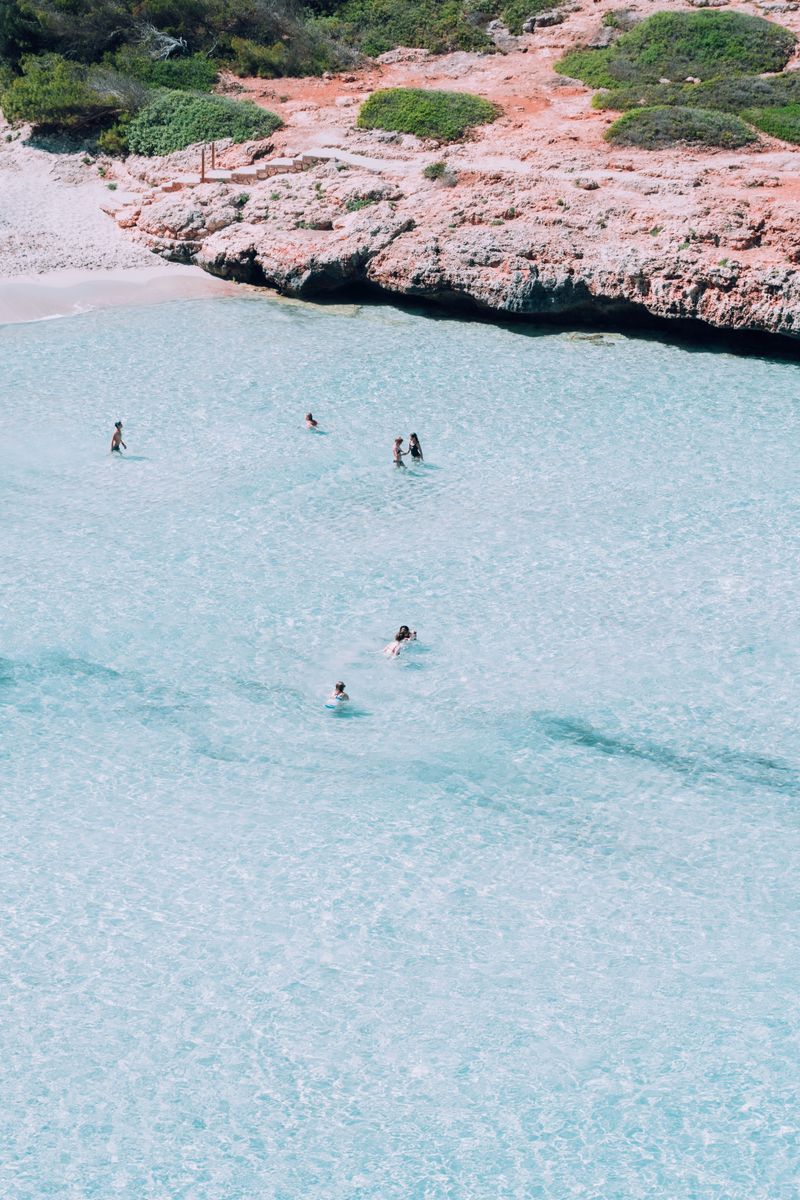 Scenic aerial view of a tranquil cove in Spain with people swimming in clear turquoise waters