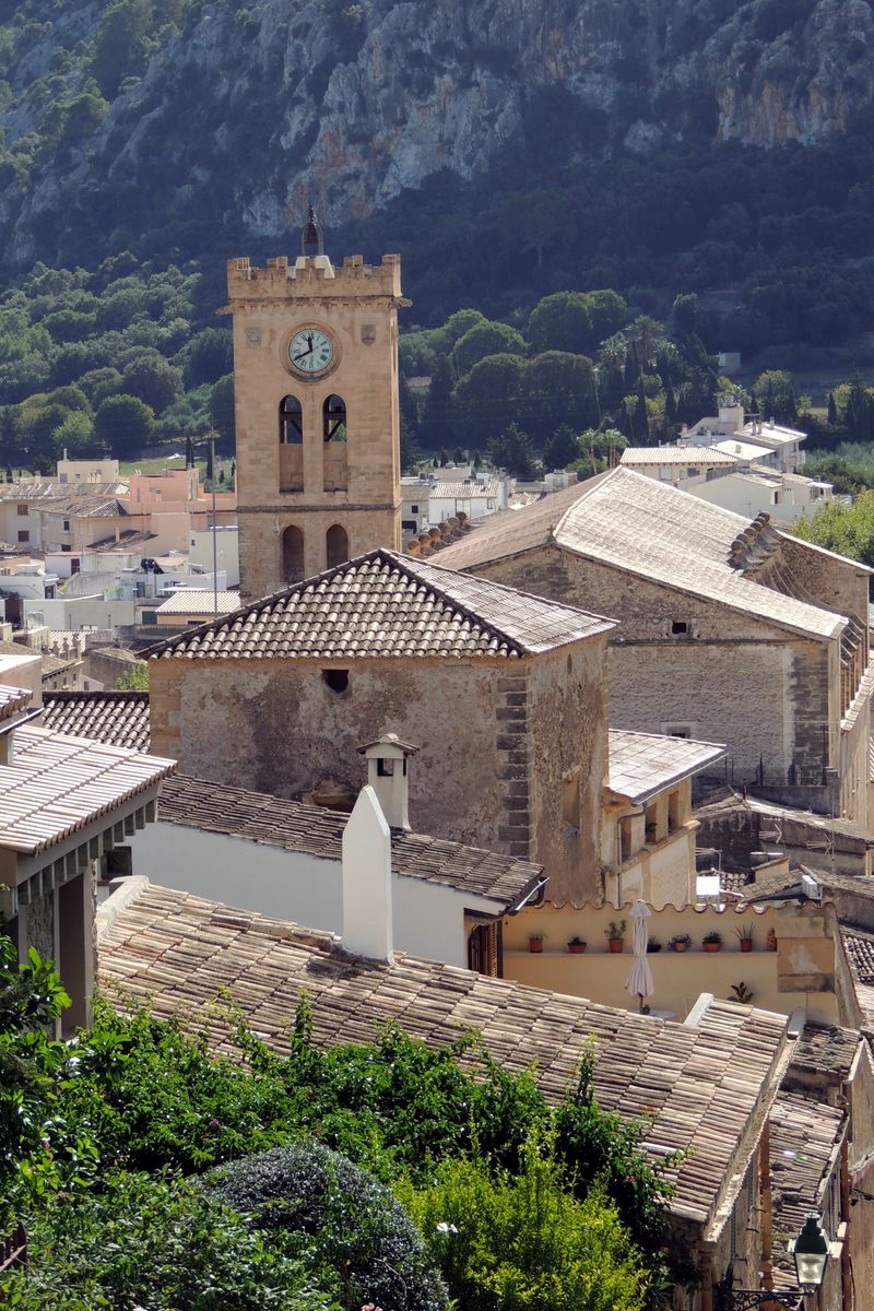 Charming aerial view of Pollença's historic center with a prominent clock tower against a lush mountain backdrop.